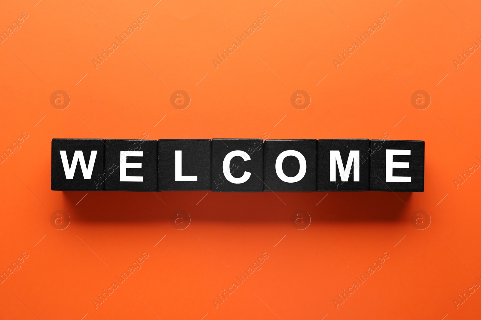 Word Welcome made of black cubes on orange background, top view Image of Word Welcome made of black cubes on orange background, top view