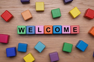 Image of Word Welcome made of colorful cubes on wooden table, flat lay