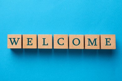 Image of Word Welcome made of wooden cubes on light blue background, top view