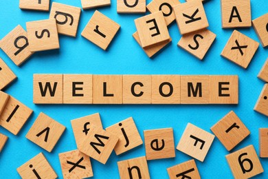 Image of Word Welcome made of wooden cubes on light blue background, flat lay