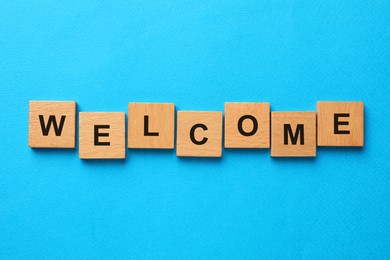 Image of Word Welcome made of wooden cubes on light blue background, top view