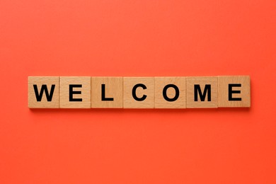 Image of Word Welcome made of wooden cubes on red background, top view