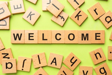 Image of Word Welcome made of wooden cubes on light green background, flat lay