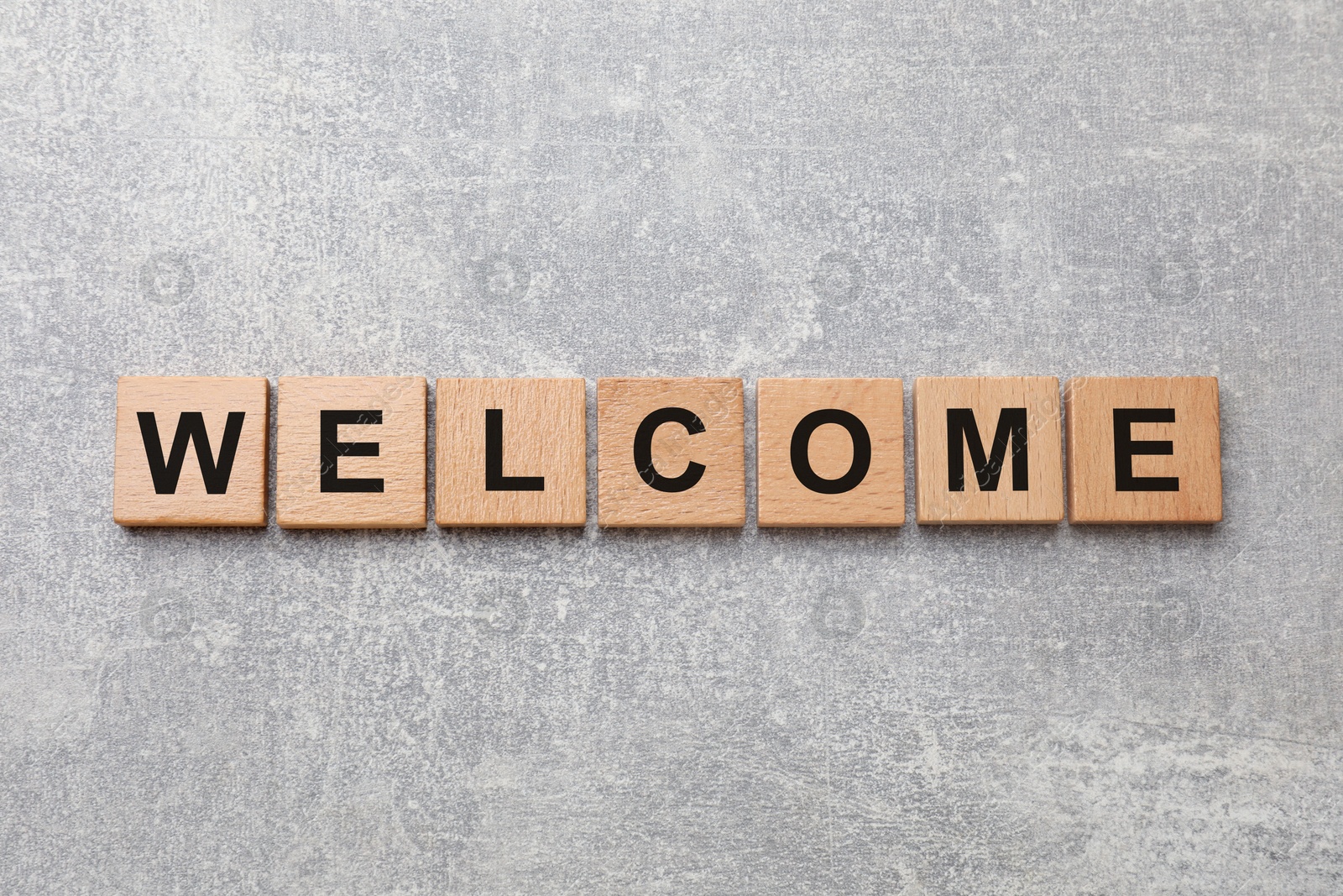Word Welcome made of wooden cubes on grey textured table, top view Image of Word Welcome made of wooden cubes on grey textured table, top view