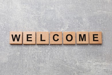 Image of Word Welcome made of wooden cubes on grey textured table, top view