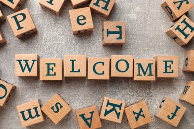 Image of Word Welcome made of wooden cubes on grey textured table, flat lay