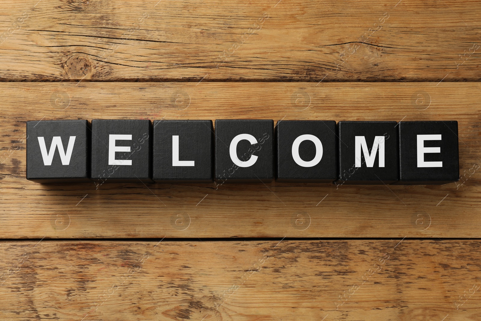 Word Welcome made of black cubes on wooden table, top view Image of Word Welcome made of black cubes on wooden table, top view