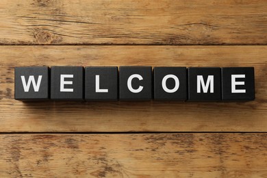Image of Word Welcome made of black cubes on wooden table, top view