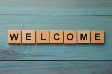 Image of Word Welcome made of wooden cubes on light blue table, top view