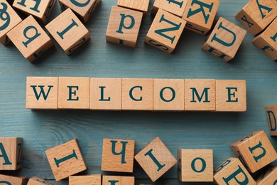 Image of Word Welcome made of wooden cubes on light blue table, flat lay