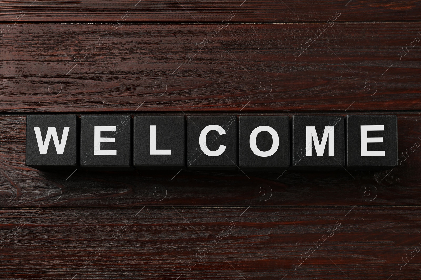 Word Welcome made of black cubes on wooden table, top view Image of Word Welcome made of black cubes on wooden table, top view