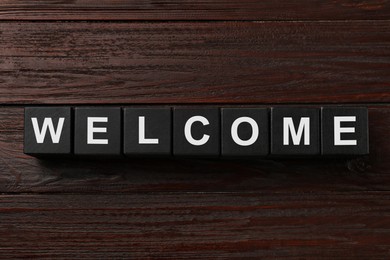 Image of Word Welcome made of black cubes on wooden table, top view