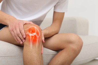 Image of Arthritis. Man suffering from pain in knee on sofa indoors, closeup. Illustration of joint inflammation on his leg