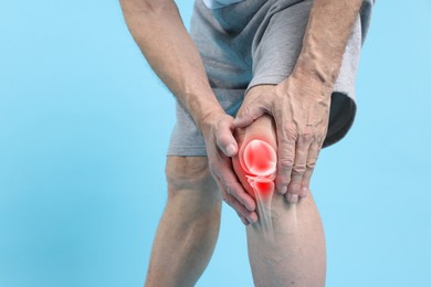 Image of Arthritis. Senior man suffering from knee pain on light blue background, closeup. Illustration of joint inflammation on his leg
