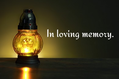 Image of In loving memory. Glowing yellow grave light on table in darkness
