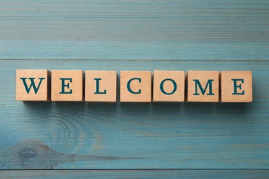 Image of Word Welcome made of wooden cubes on light blue table, top view