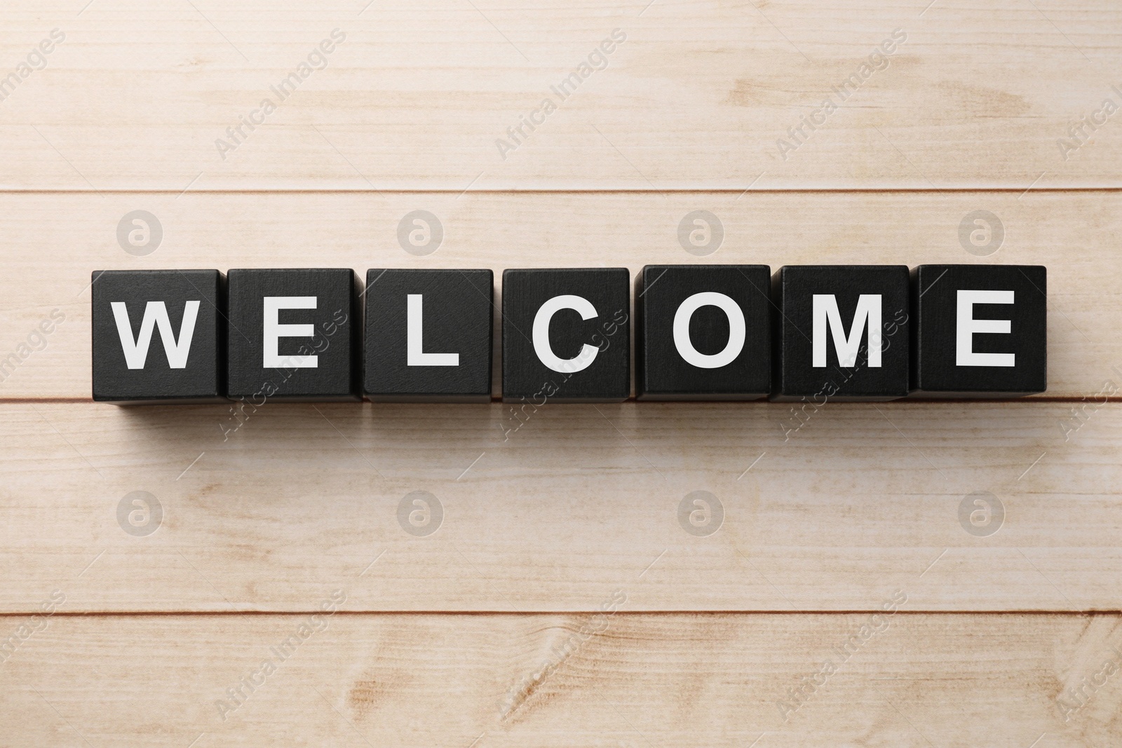 Word Welcome made of black cubes on light wooden table, top view Image of Word Welcome made of black cubes on light wooden table, top view