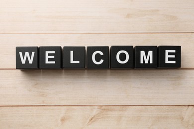 Image of Word Welcome made of black cubes on light wooden table, top view