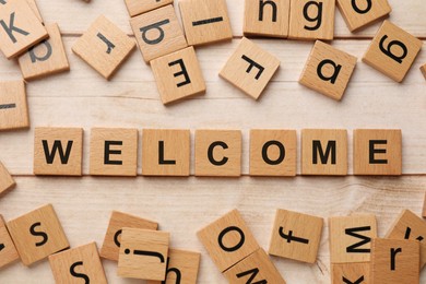 Image of Word Welcome made of wooden cubes on light table, flat lay