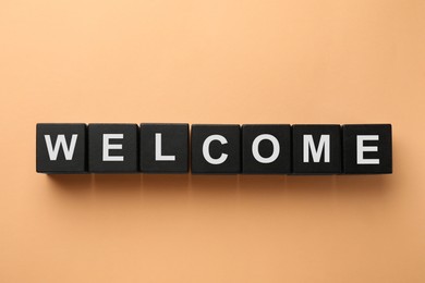 Image of Word Welcome made of black cubes on beige background, top view