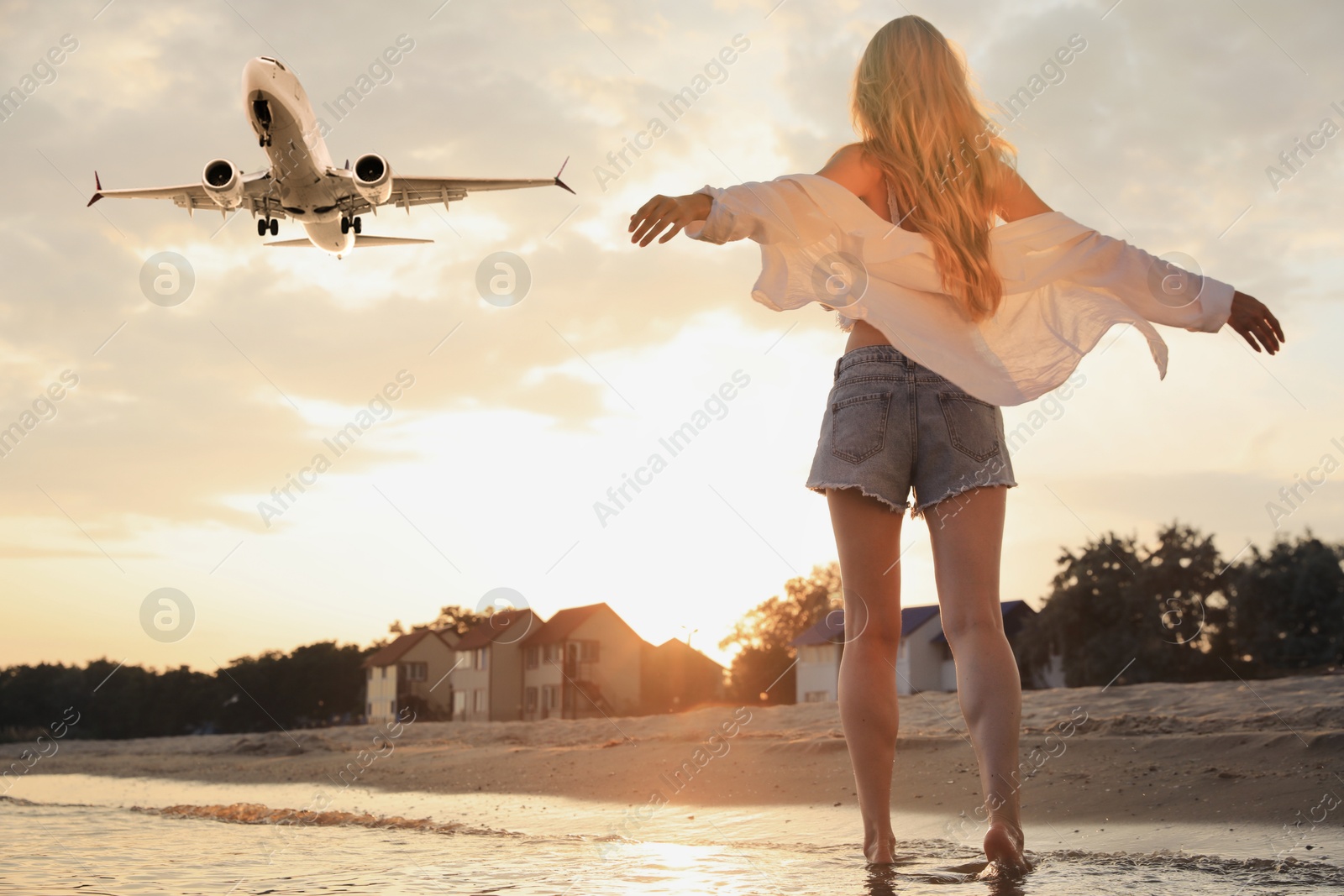 Woman on sandy beach looking at airplane flying in sky, back view Image of Woman on sandy beach looking at airplane flying in sky, back view