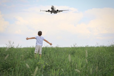 Image of Little boy in green field looking at airplane flying in sky, back view