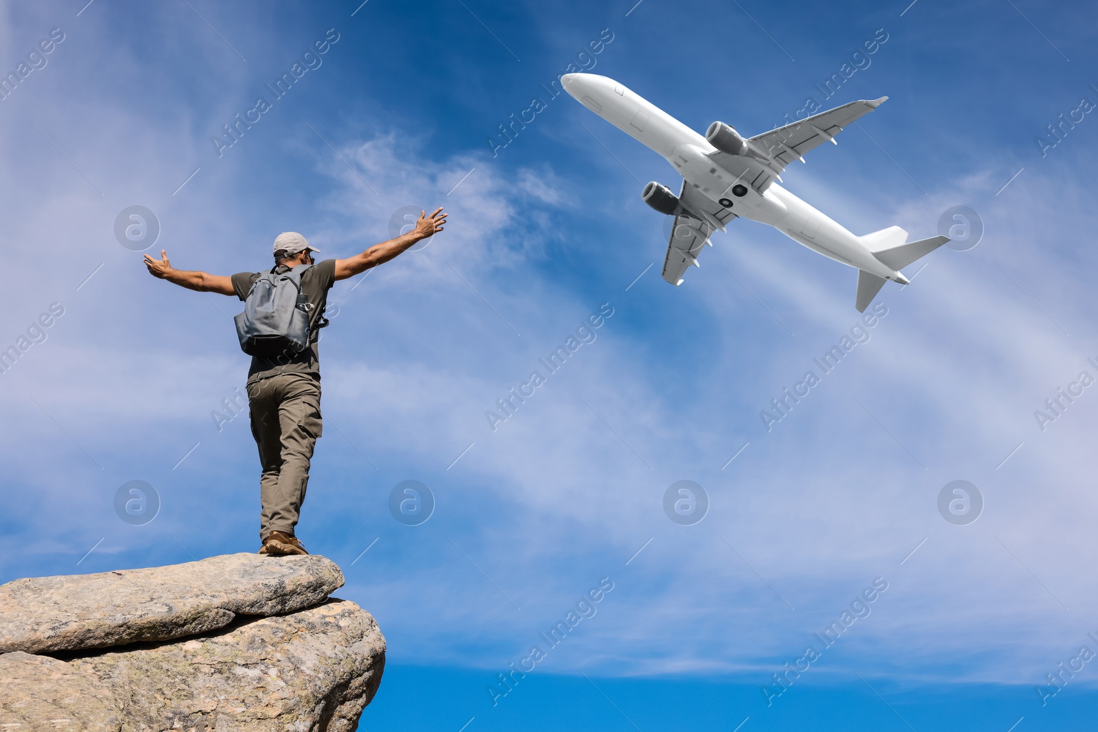 Man on rocky peak looking at airplane flying in sky, back view Image of Man on rocky peak looking at airplane flying in sky, back view