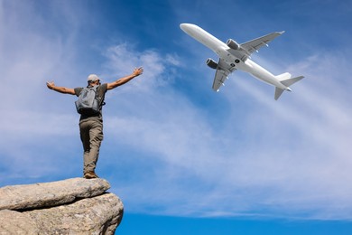 Image of Man on rocky peak looking at airplane flying in sky, back view