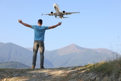 Image of Man in mountains looking at airplane flying in sky, back view