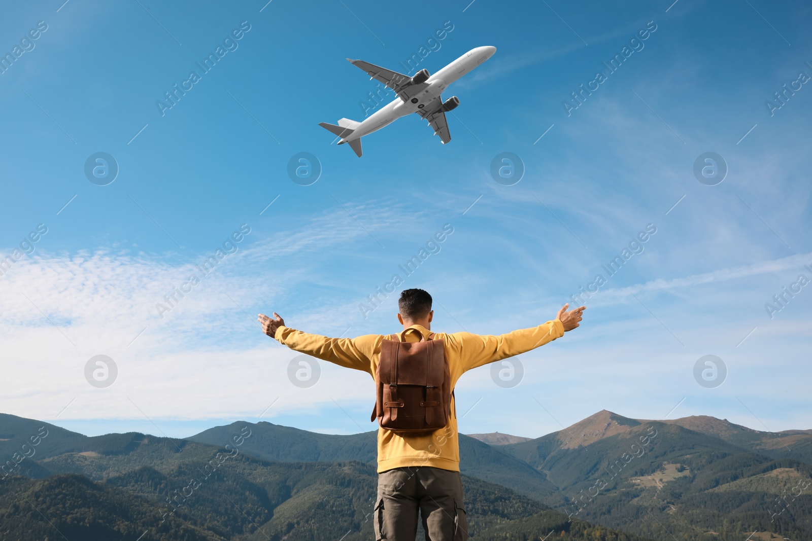 Image of Man in mountains looking at airplane flying in sky, back view