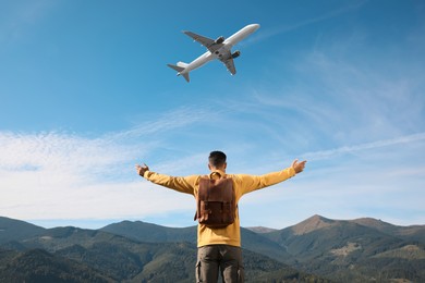 Image of Man in mountains looking at airplane flying in sky, back view