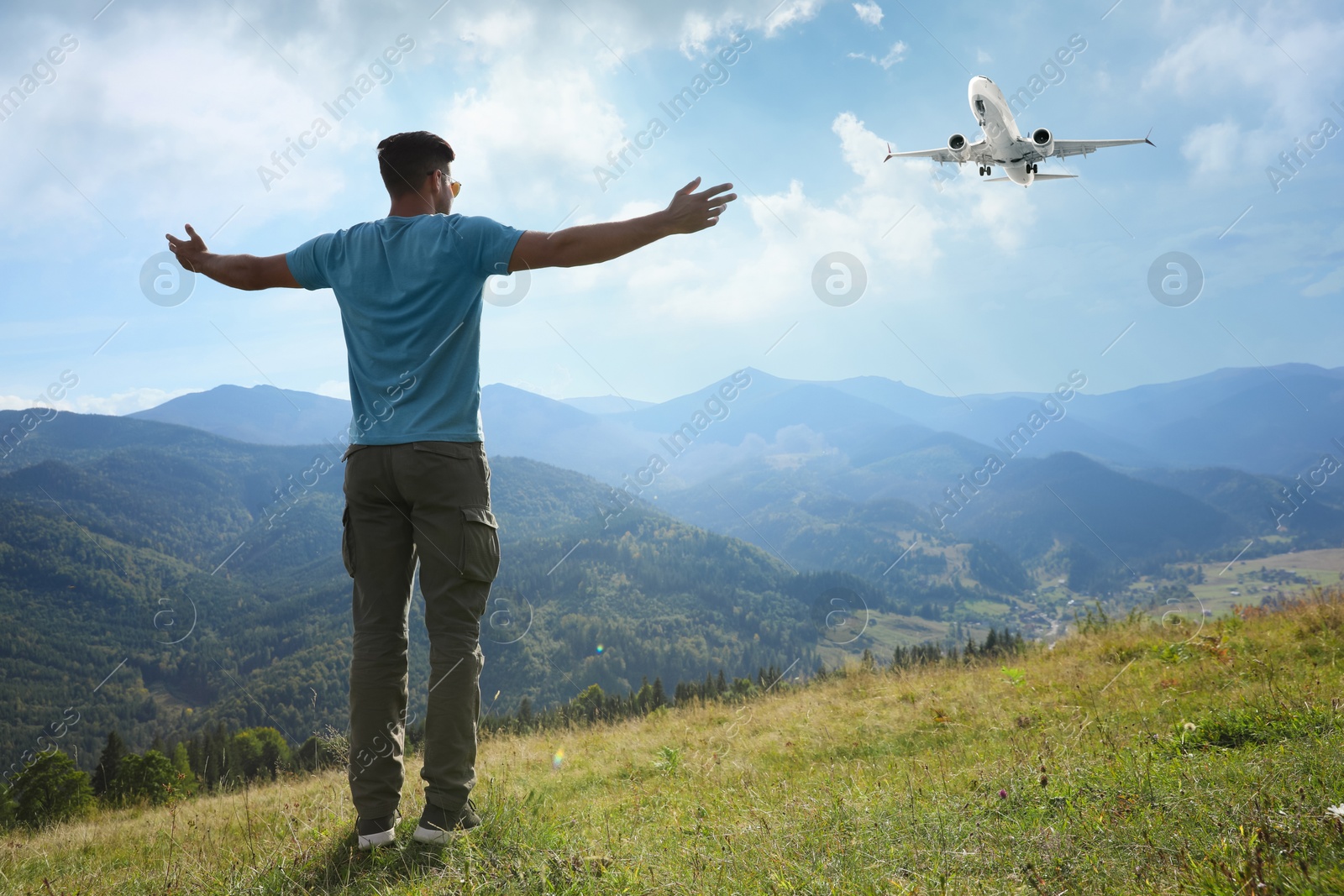 Image of Man in mountains looking at airplane flying in sky, back view