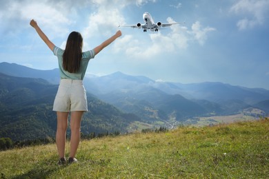 Image of Woman in mountains looking at airplane flying in sky, back view