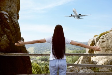 Image of Woman in mountains looking at airplane flying in sky, back view