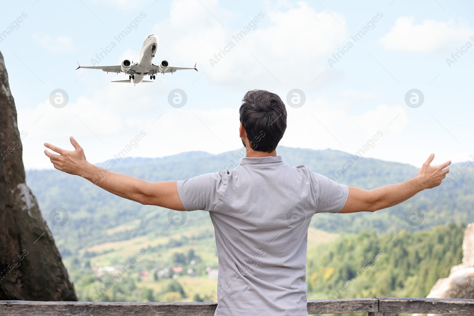 Image of Man in mountains looking at airplane flying in sky, back view