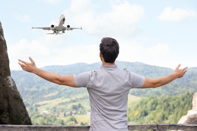 Image of Man in mountains looking at airplane flying in sky, back view