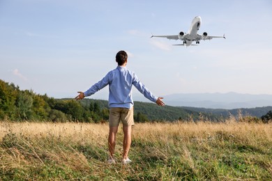 Image of Man in mountains looking at airplane flying in sky, back view
