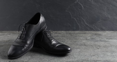 Photo of Pair of black leather shoes on grey surface, closeup. Space for text