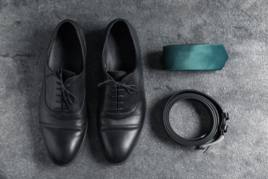 Photo of Pair of black leather shoes, belt and necktie on grey surface, flat lay