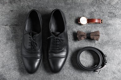 Photo of Pair of black leather shoes, wrist watch, belt and bow tie on grey surface, flat lay