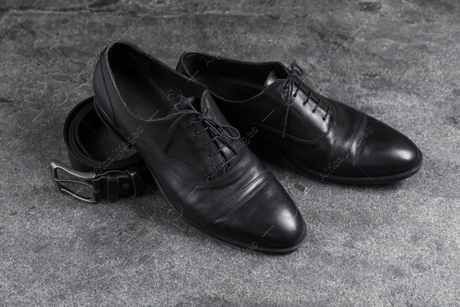 Photo of Pair of black leather shoes and belt on grey surface