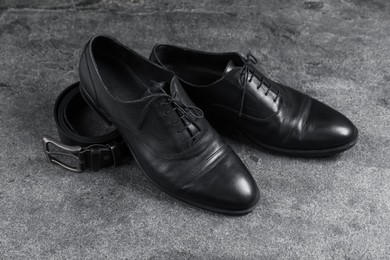 Photo of Pair of black leather shoes and belt on grey surface
