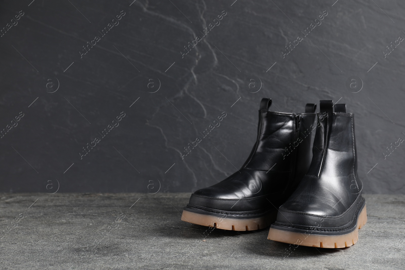 Pair of stylish black boots on grey surface, space for text Photo of Pair of stylish black boots on grey surface, space for text