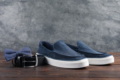 Photo of Pair of dark blue shoes, belt and bow tie on wooden surface