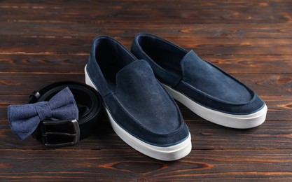 Photo of Pair of dark blue shoes, belt and bow tie on wooden surface, closeup