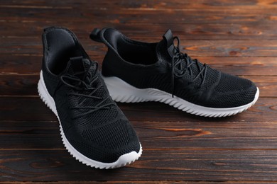 Photo of Pair of black sneakers on wooden surface, closeup