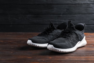 Photo of Pair of black sneakers on wooden surface, closeup. Space for text