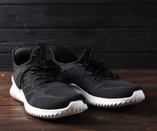 Photo of Pair of black sneakers on wooden surface, closeup