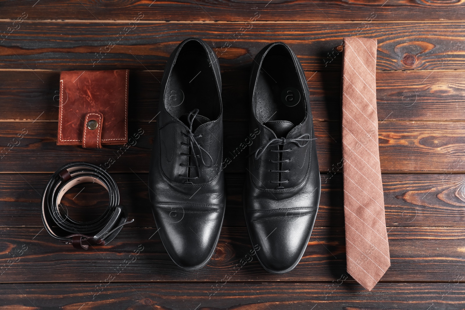 Photo of Pair of black leather shoes, necktie, belt and purse on wooden table, flat lay