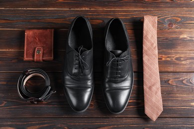 Photo of Pair of black leather shoes, necktie, belt and purse on wooden table, flat lay